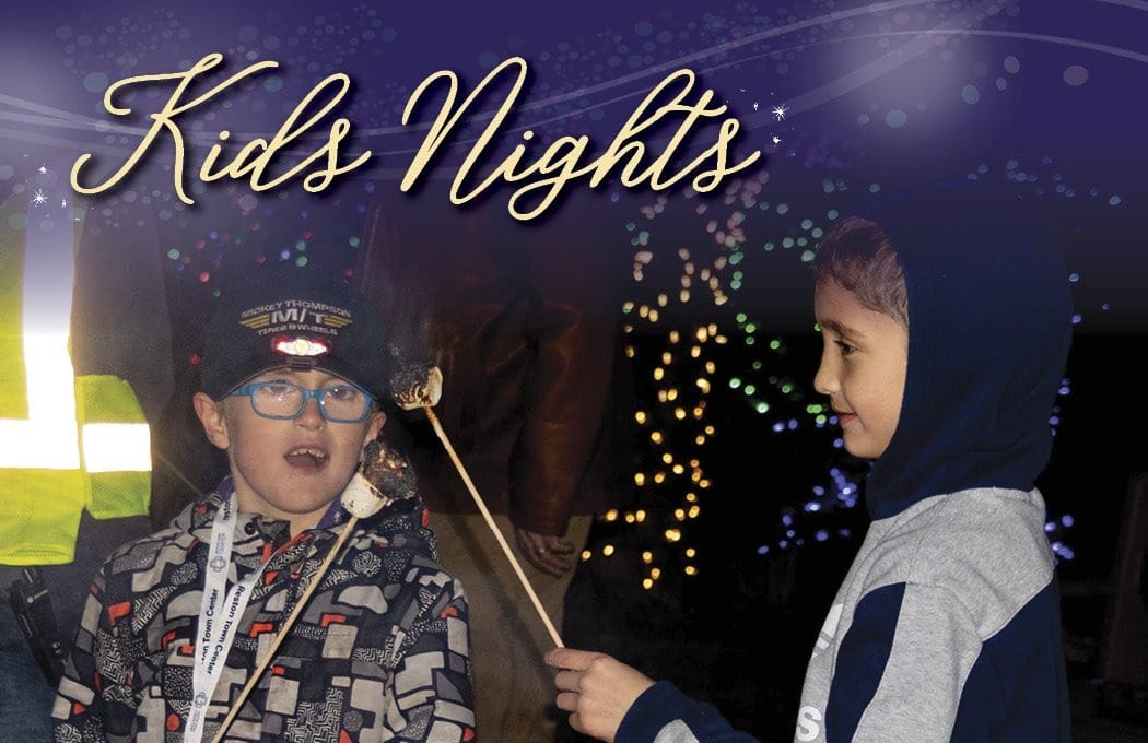 Two kids roasting marshmallows at night, lights in the background.