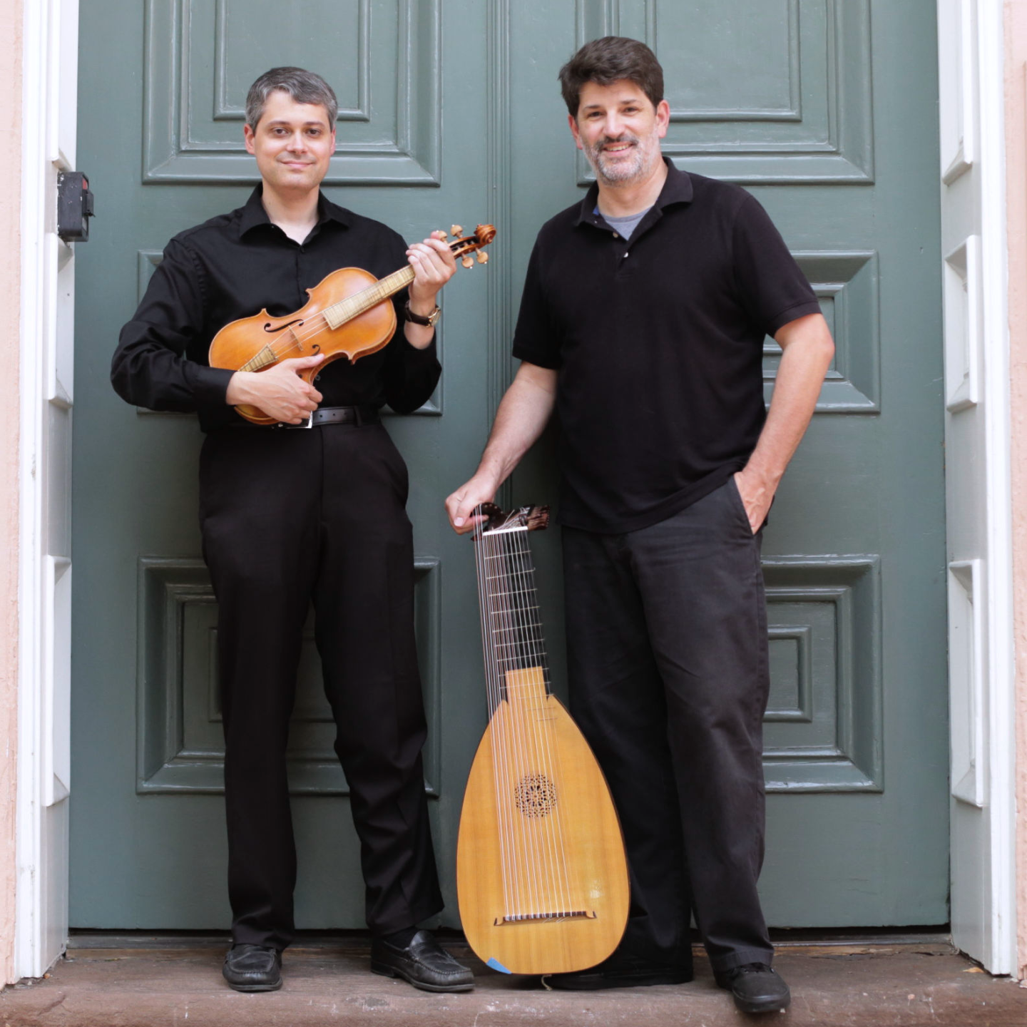 Two men with instruments stand in front of large double doors.